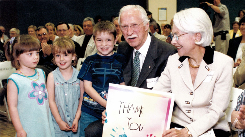 Elderly couple holds up a thank you sign given to them by three children