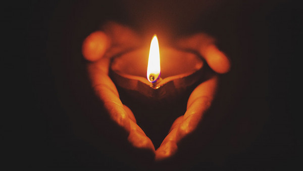 hands holding a lit candle, with the shadows forming a heart shape with the hands