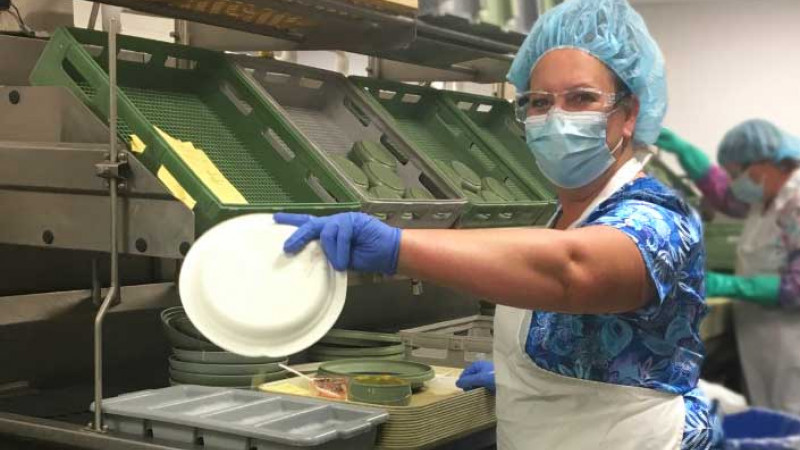 A food service worker holding a plate in a hospital kitchen
