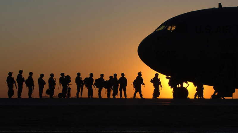silhouette of soldiers boarding a plane with a the sky in sunset orange behind them