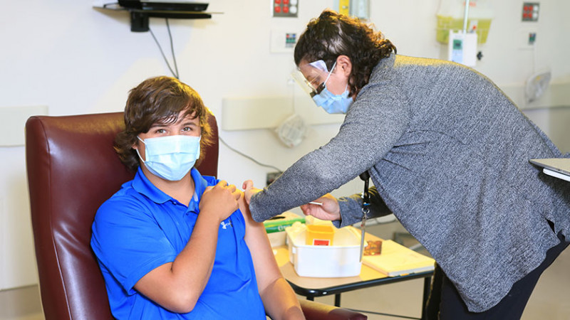 teenage boy receiving a COVID-19 vaccination from a female clinician