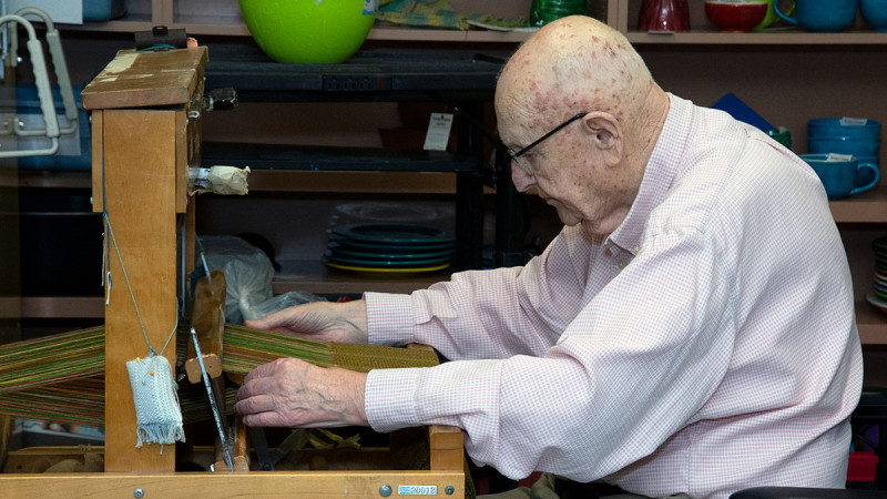an elderly Veteran creating an art piece at a weaving loom