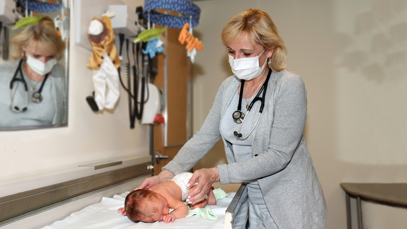 Dr. Laura Lyons holding an infant on an examination table in her office