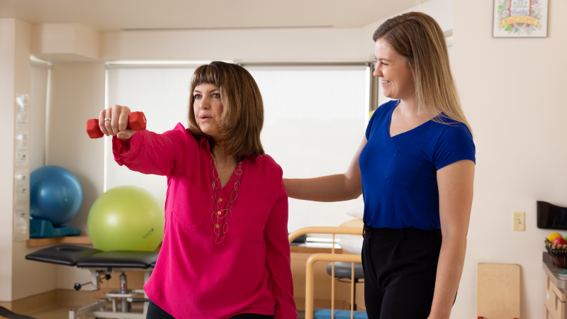 Woman raising a dumbell with care provider's support