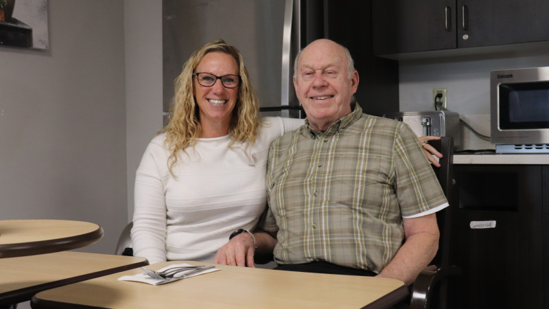 Jennifer Field in a cream sweater sits with Veteran Joseph "Lou" Warren in a plaid shirt at a dining table