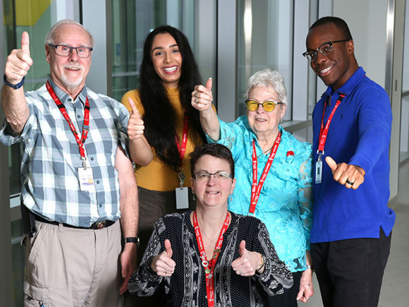 a group of two men and three women volunteers each showing a thumbs up