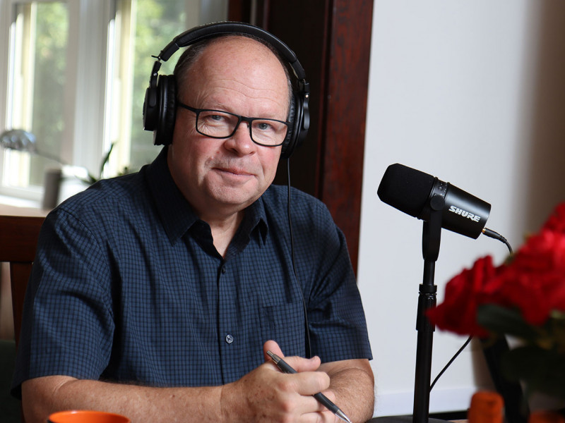 Ian Gillespie wearing a headset sitting a table in front of a microphone on a stand
