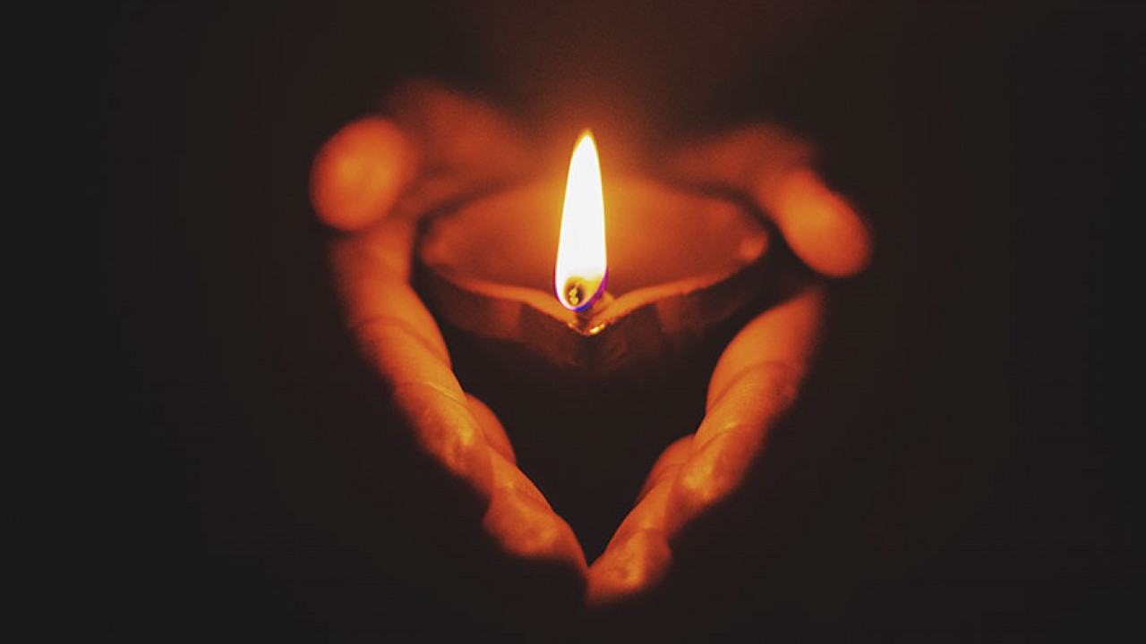 hands holding a lit candle, with the shadows forming a heart shape with the hands