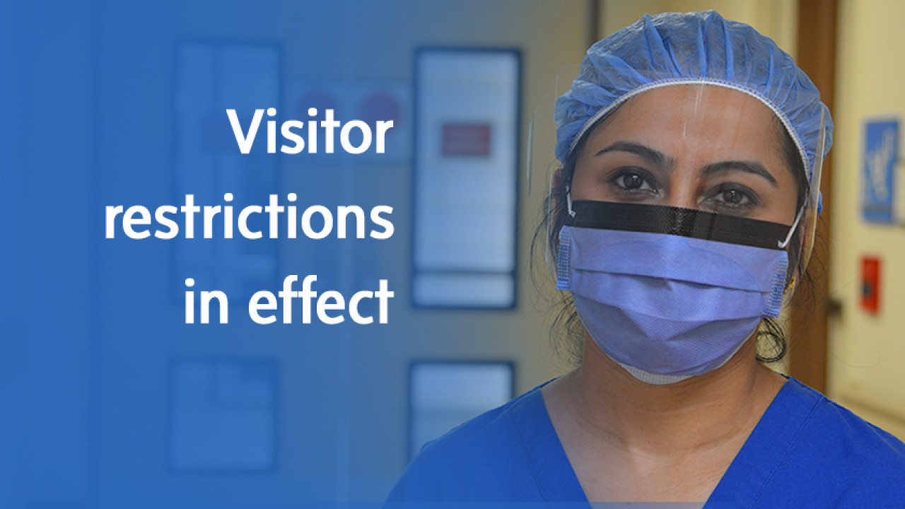 a nurse wearing a face shield and medical mask with a graphic that reads: Visitor restrictions in effect