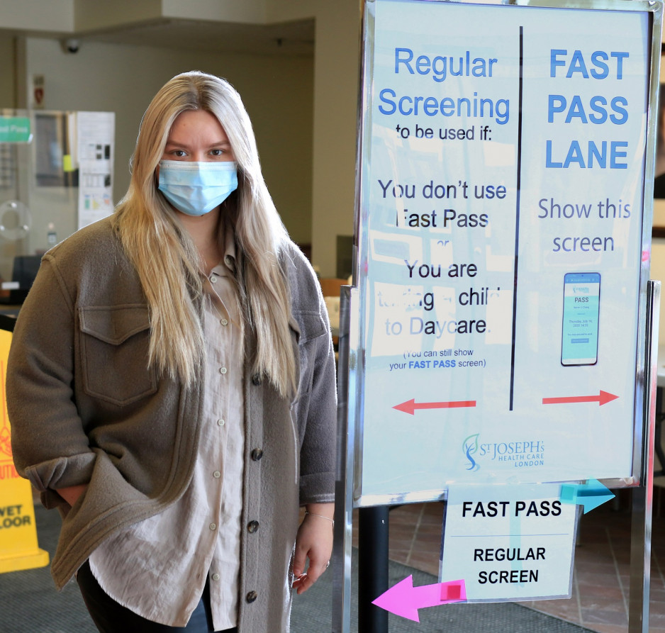 Woman wearing mask standing next to sign directing visitors to screening