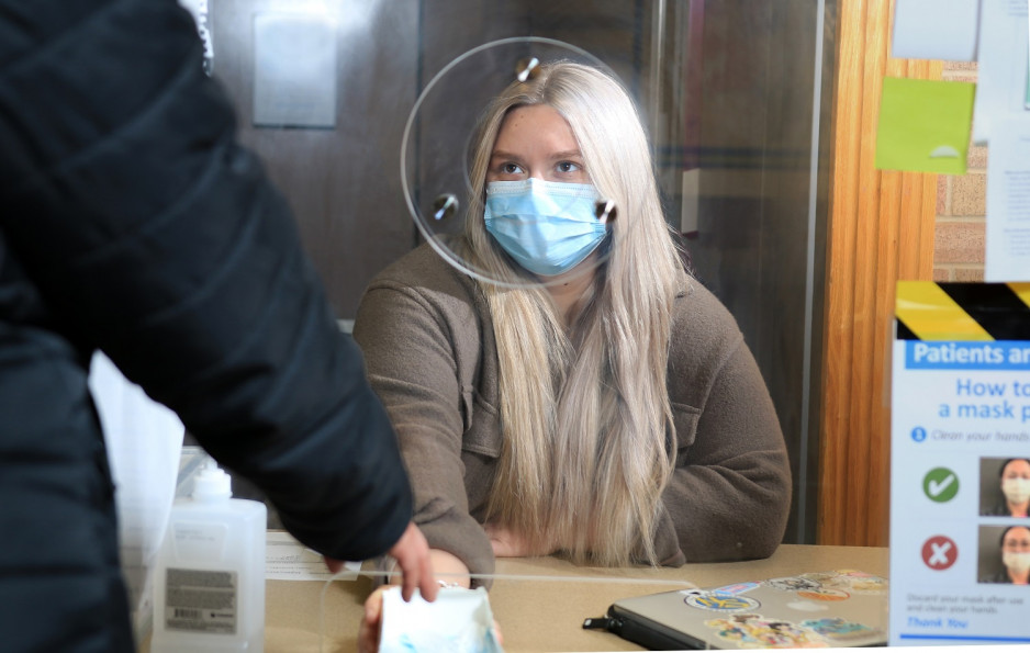 woman wearing a mask hands box of surgical masks to visitor