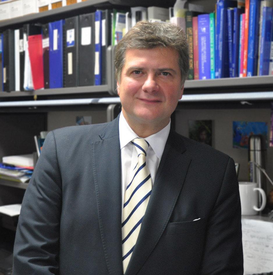 Dr. Manuel Montero-Odasso wearing a suit and tie, standing in front of a wall of books