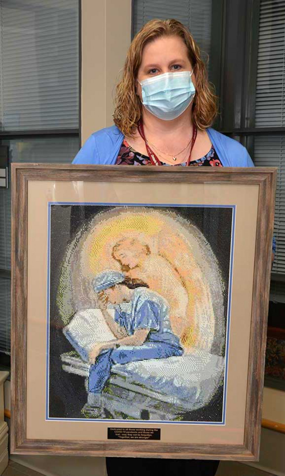 A nurse holding a painting of a nurse with an angel touching her shoulder. 