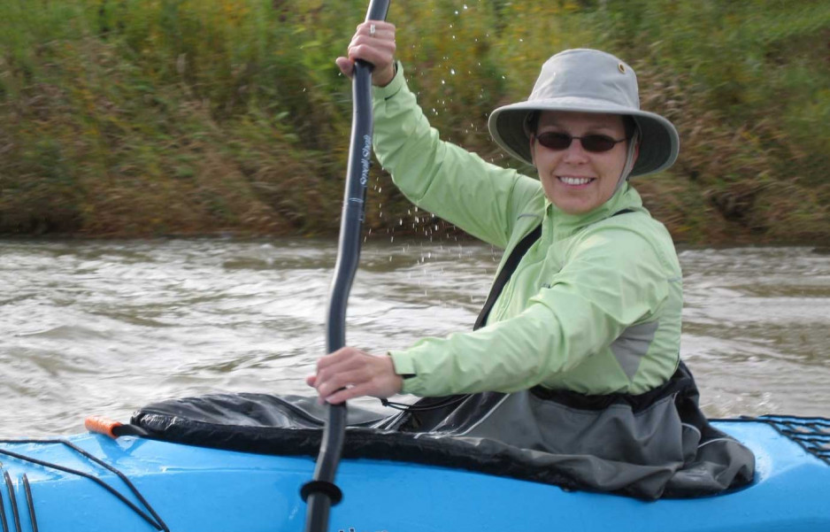 Lori Linton paddling a kayak, wearing sunglasses and a hat, smiling 
