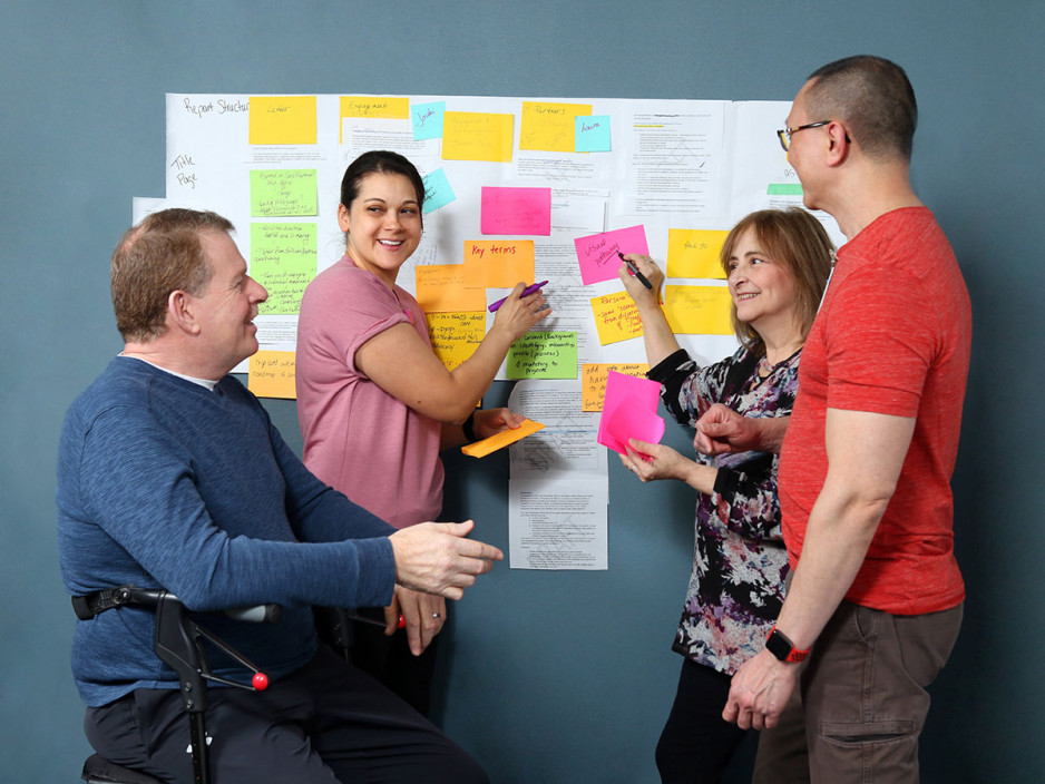 two men and two women in front of a board with post-it notes, sharing their ideas