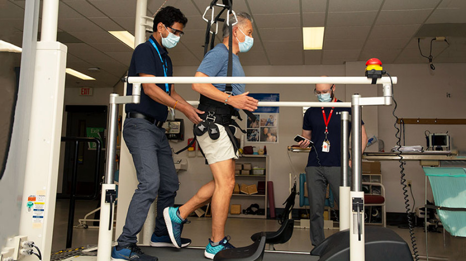 patient Michael Kan running on a treadmill supported by a harness and a physiotherapist