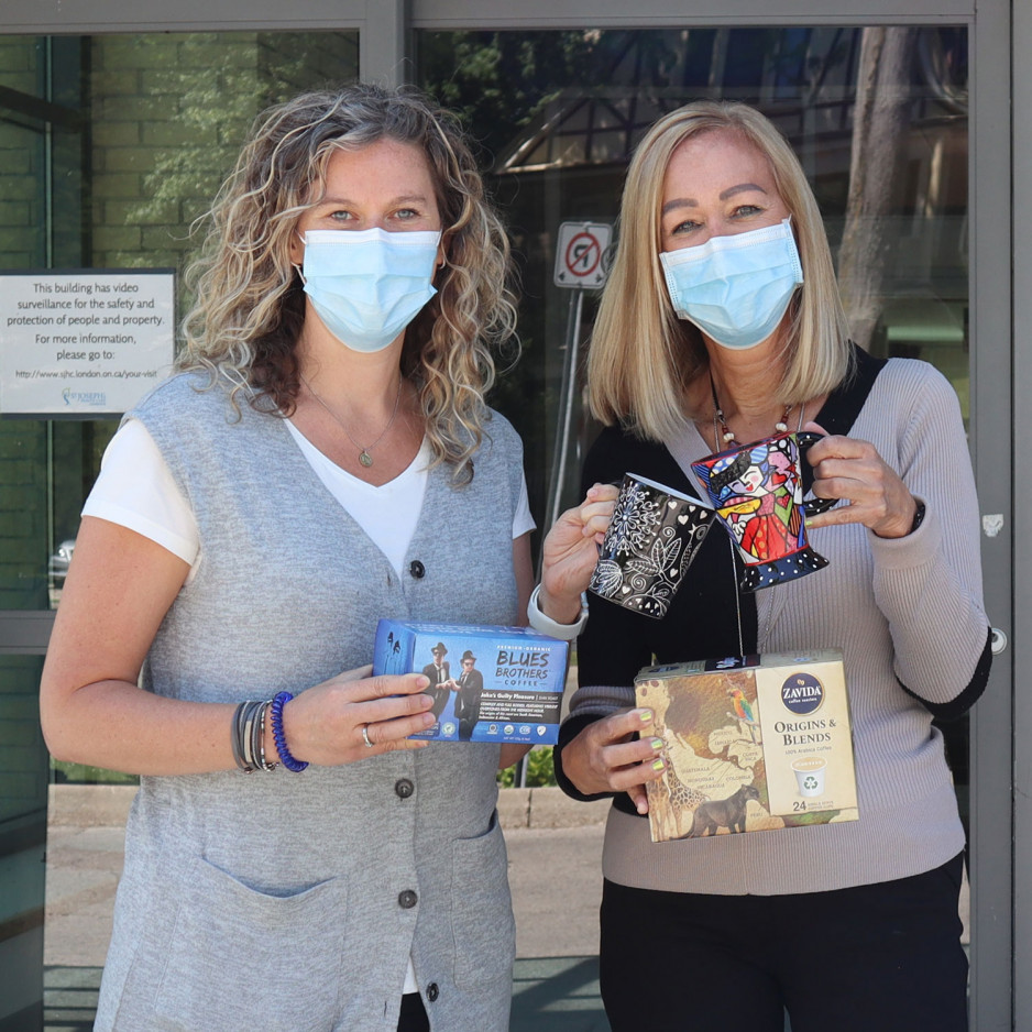 two women wearing masks hold up boxes of snacks