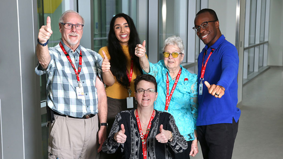 a group of two men and three women volunteers each showing a thumbs up