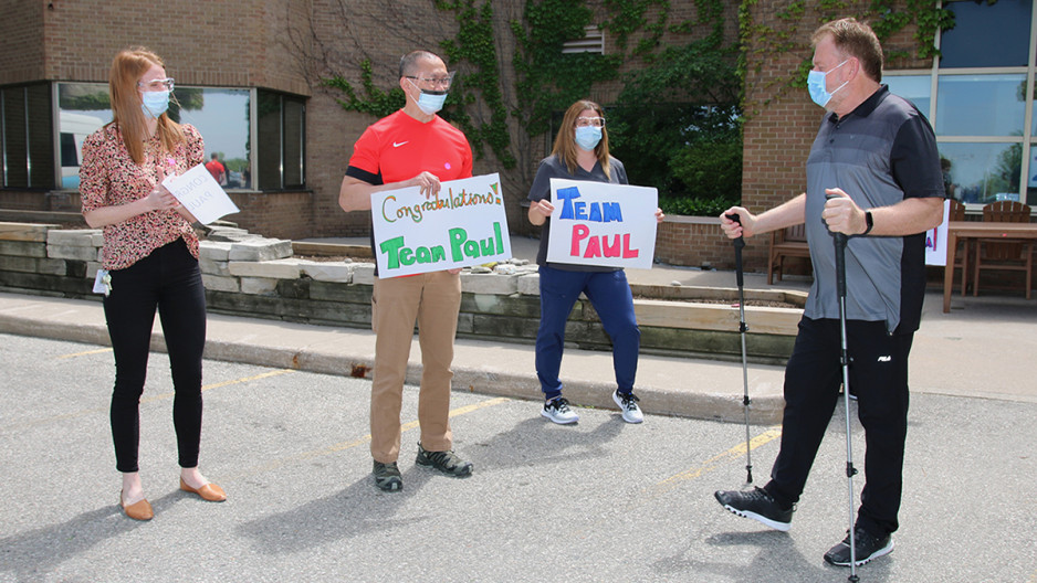 A patient leaves Parkwood Institute with his physiotherapists holding signs that cheer him on