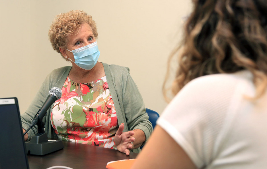 Wendi Heal wearing a mask and sitting in front of a microphone speaking to her therapist seen in the foreground from behind