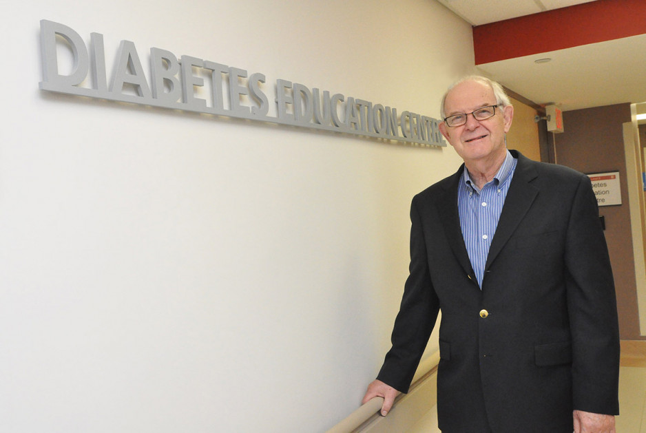 An elderly man in glasses and a dark suit with a blue dress shirt stands beside a sign that says, "Diabetes Education Centre".