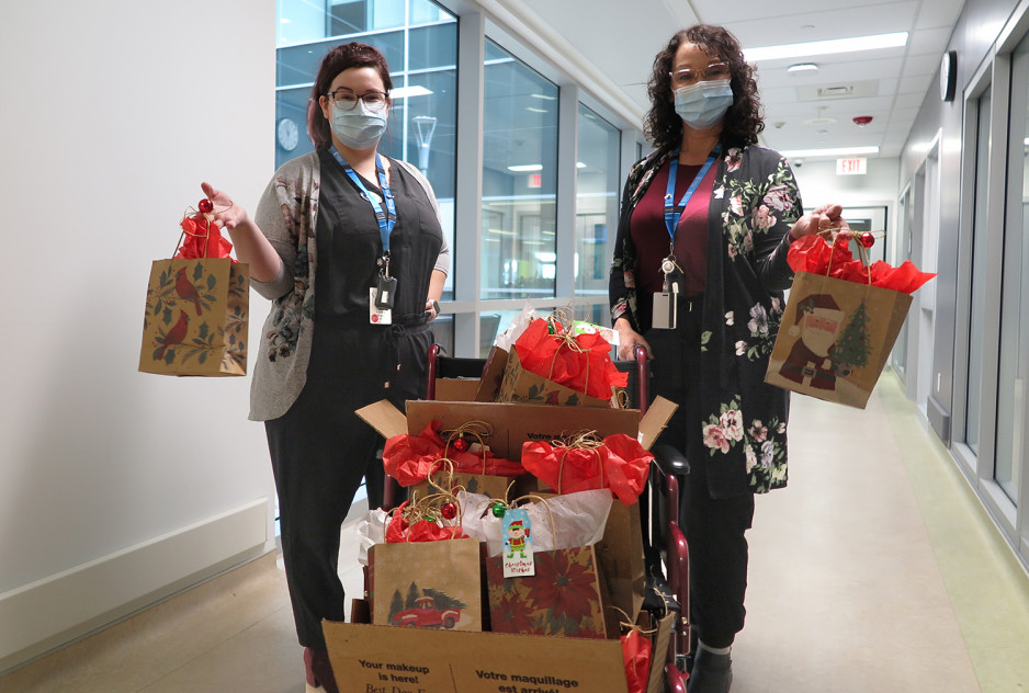 nurses Lyndsey Wintle and Kelly Hovorka holding gift bags, surrounded by a pile of Christmas gift bags