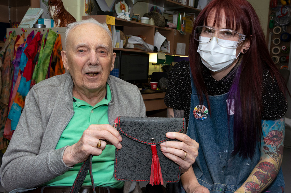 Veteran John Spivey displaying a handmade purse with art instructor Kim Smith sitting beside him.