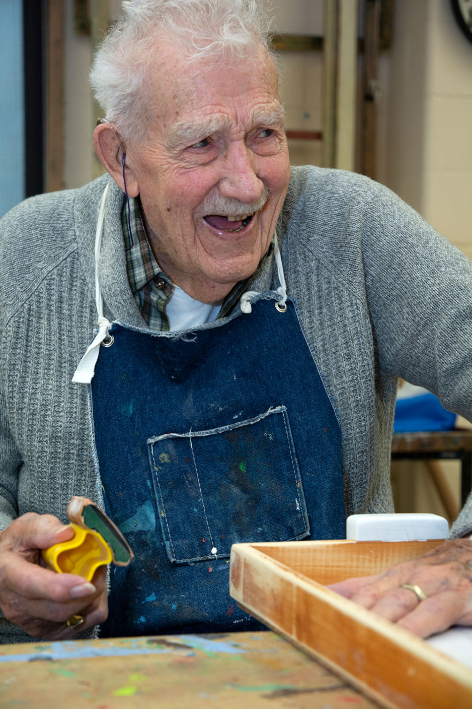 Veteran Charles Astles smiling as he sands a woodworking project by hand