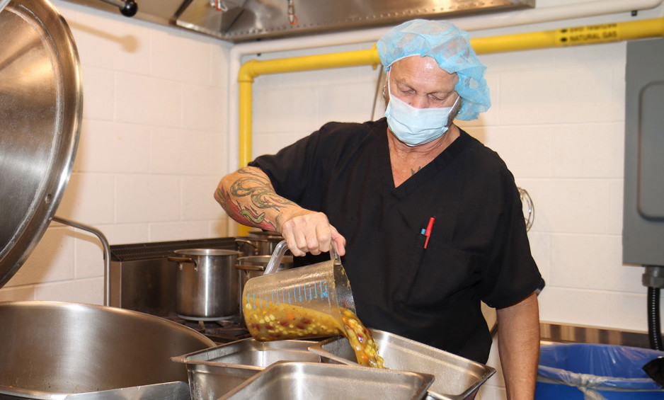 A chef wearing an apron, mask and hairnet pouring Three Sisters Soup into a serving tray in the kitchen at Parkwood Insitute