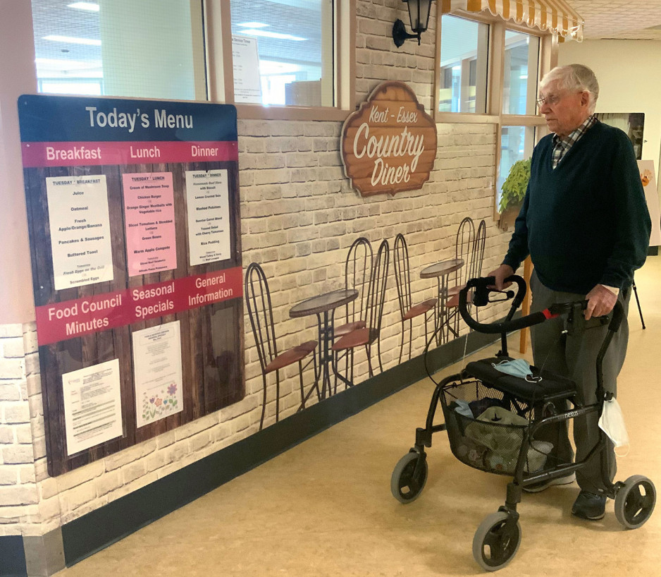 a veteran using a walker standing in front of a menu board showing what meals are being served