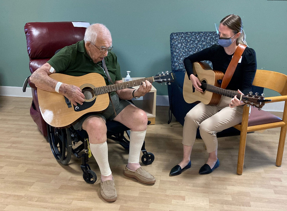 a veteran playing the guitar, instructed by a music instructor who is also playing a guitar
