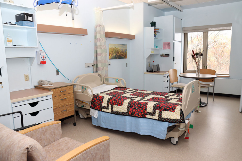 the Palliative Care and Comfort room in the Veterans Care Program painted in pale blue with a quilt on the hospital bed, a table for two and an upholstered chair