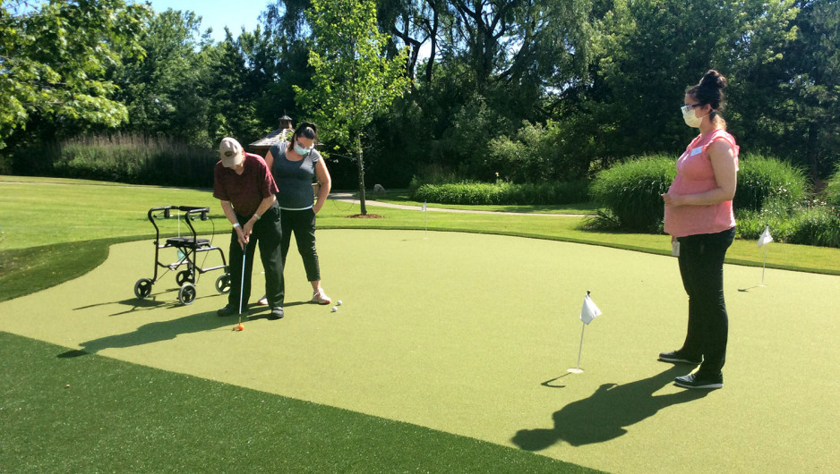 a veteran putting on a putting green with a staff member at his side and another staff member standing near the hole