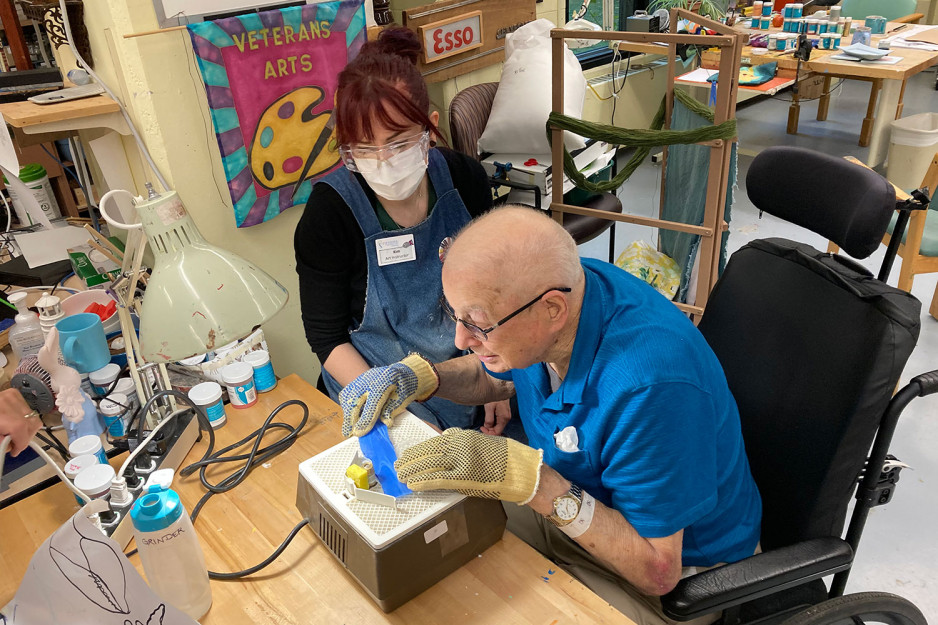 a veteran working on an art project at a table supervised by an art instructor