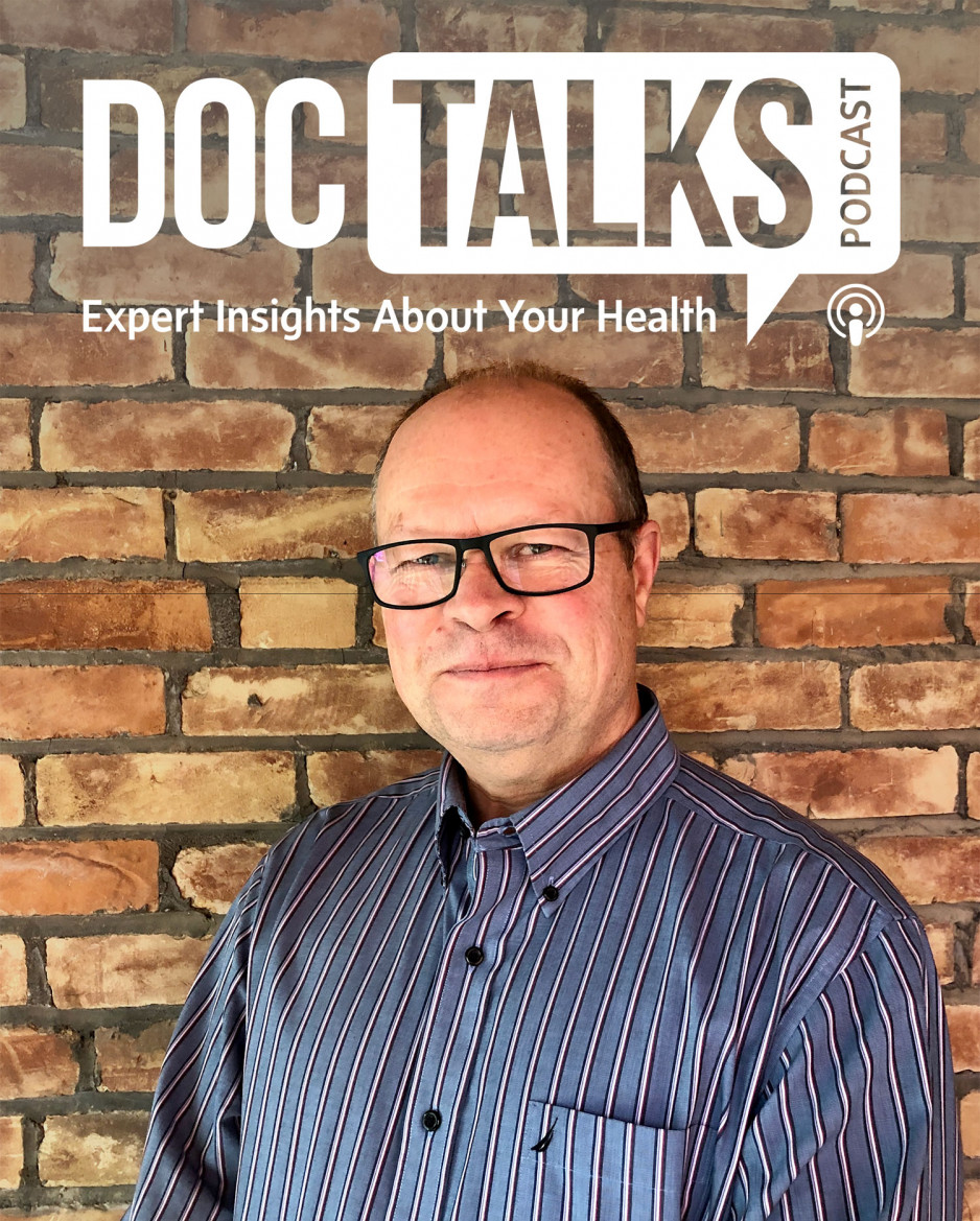 Ian GIllespie standing next to a brick wall with the DocTalks Podcast logo over his head