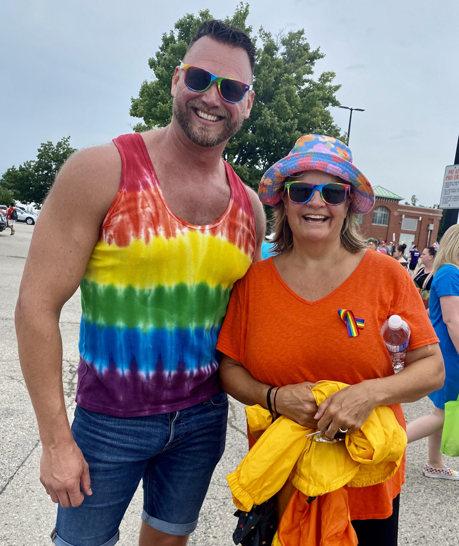 a man wearing a pride-striped shirt and sunglasses standing next to a woman wearing a pride pin and brightly coloured clothing