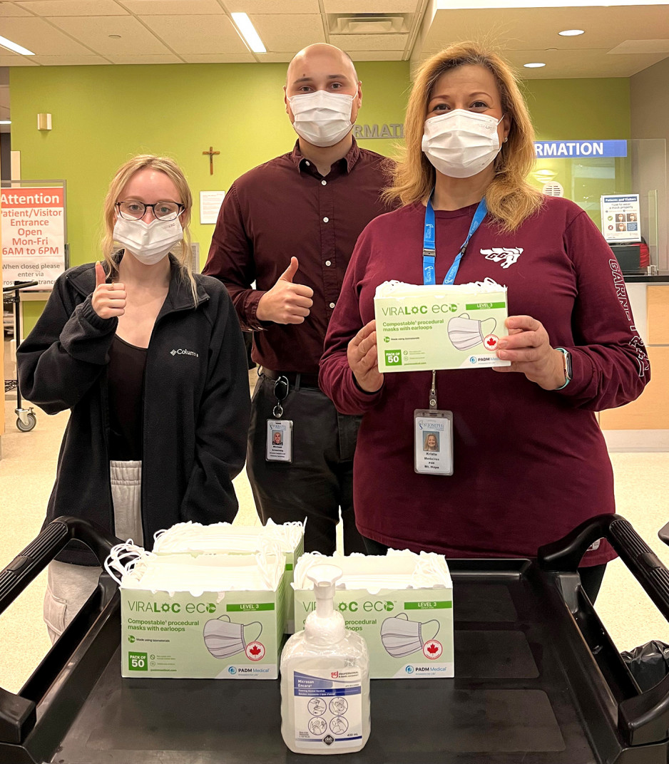 three staff members wearing masks standing in front of a cart with boxes of new bio masks