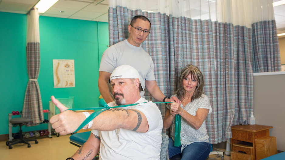 male patient does exercises with a rubber band while two others observe