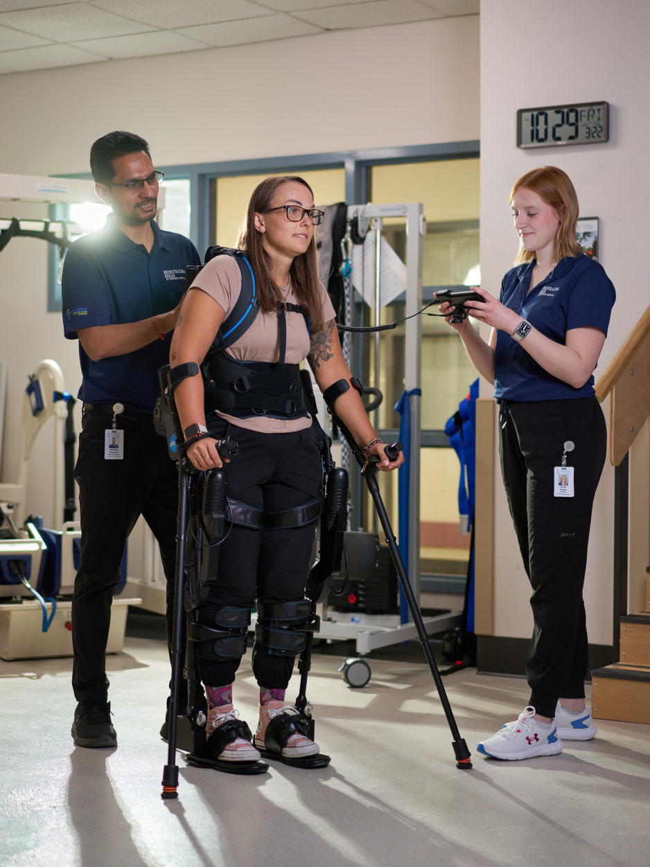 A woman walks with the assistance of the Ekso supported by two physiotherapists