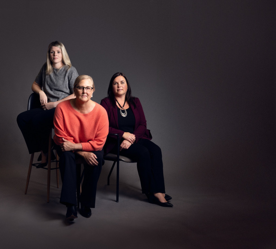 Three people sitting in chairs in front of a grey backdrop