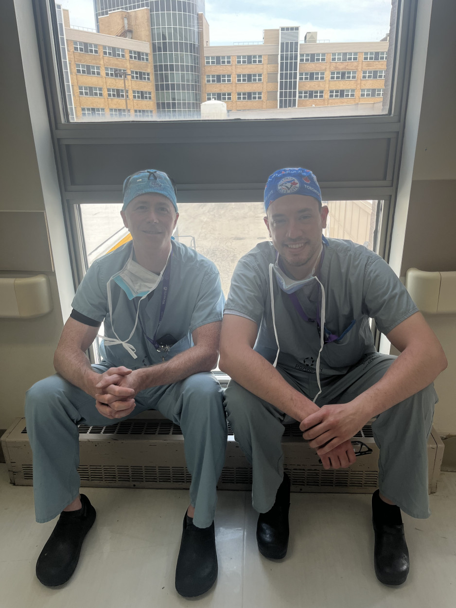 Two health care providers in scrubs sit in front of a window
