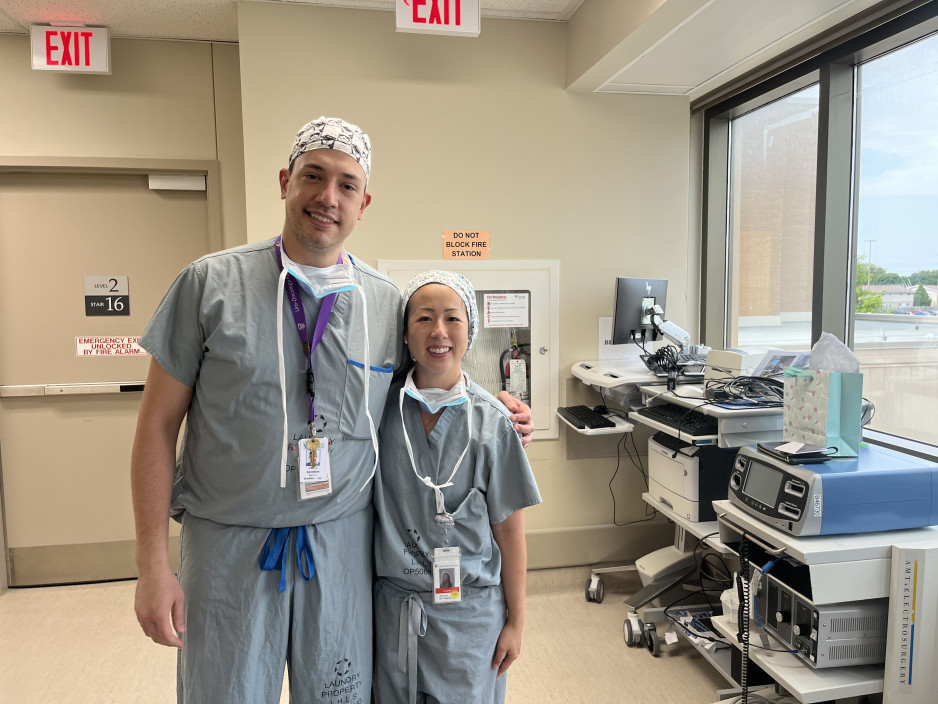 Two health care providers stand smiling in their scrubs