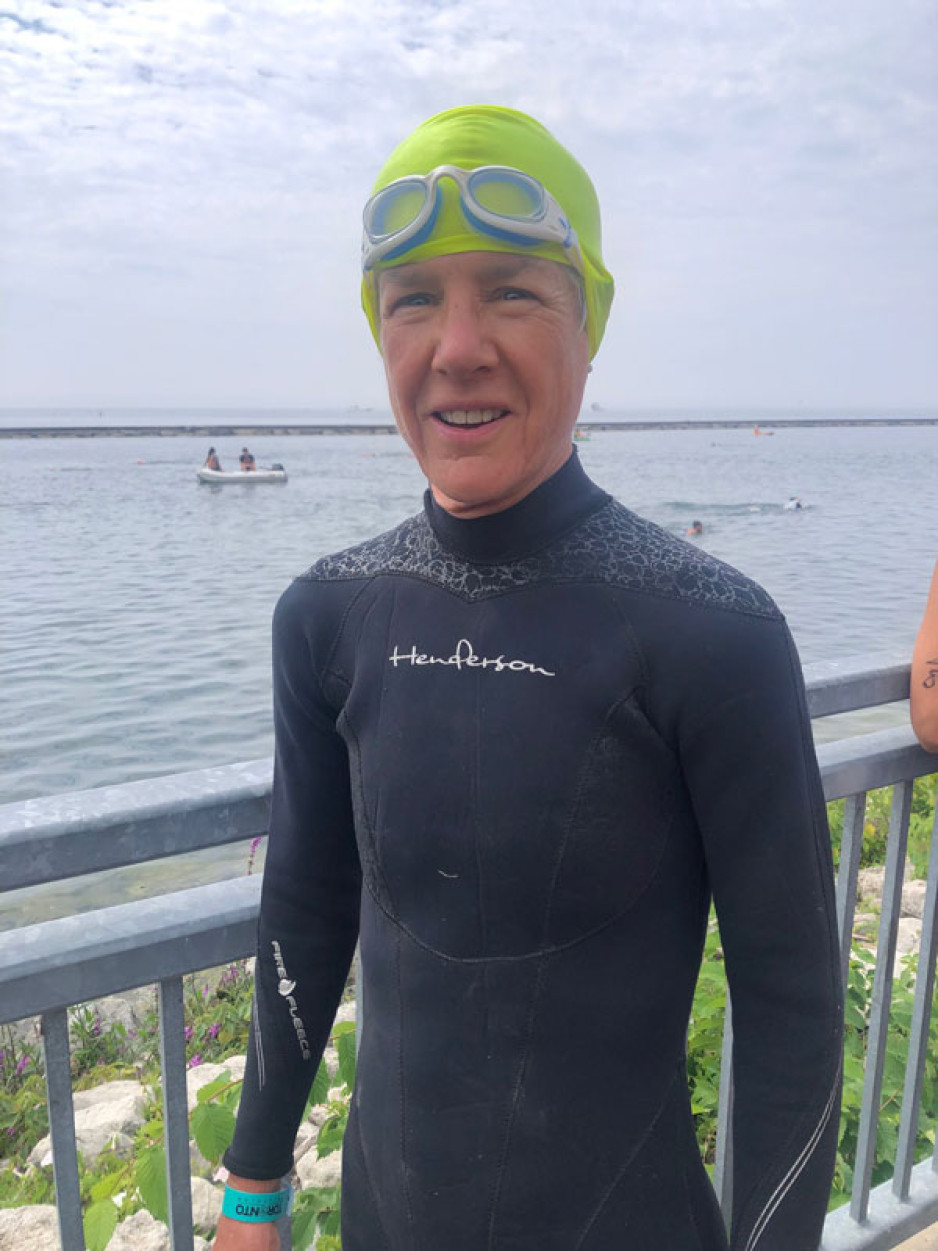 Janet Tufts with neoprene bath suit in front of a lake, ready to swim