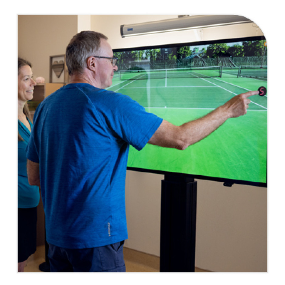 Andrew Fuller points at a large screen displaying a virtual tennis court, with a tennis ball highlighted,