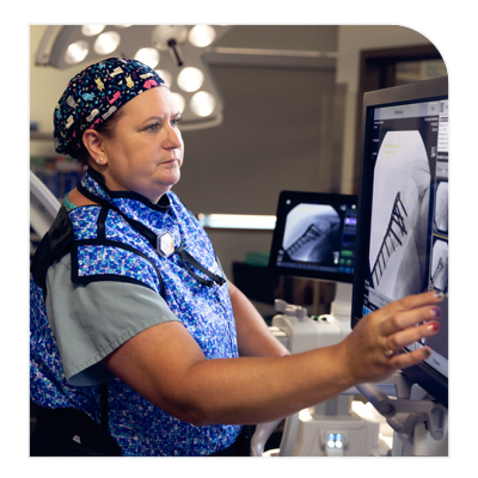 A surgeon in a blue patterned cap and scrubs points at a monitor