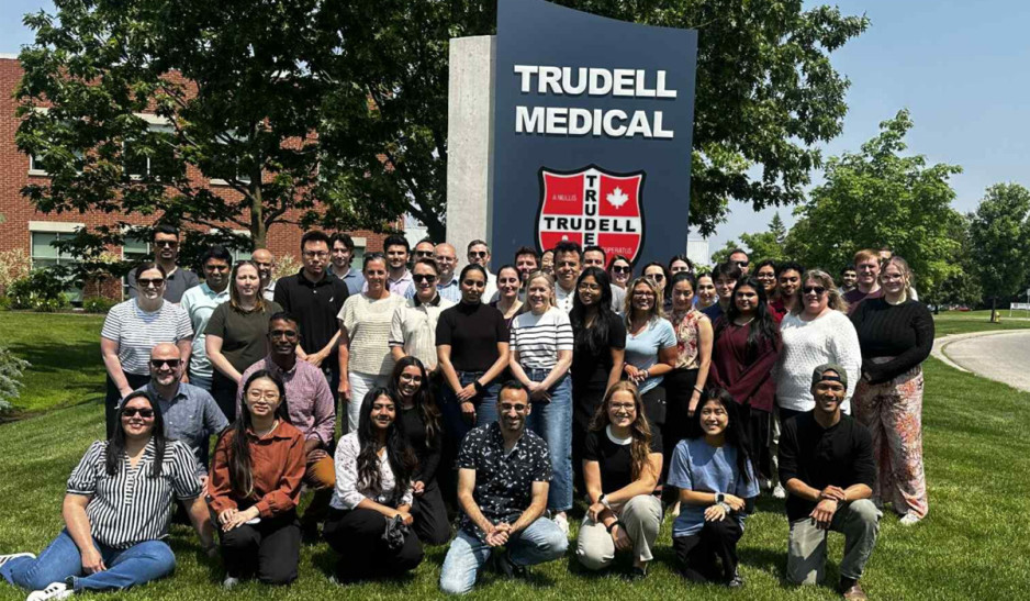 Trudell employees posing for a photo on a grassy area in front of Trudell building