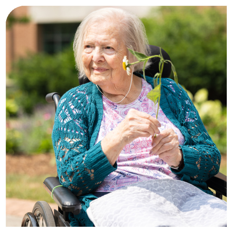 Helga holding a plant with her hands sited on her wheelchair