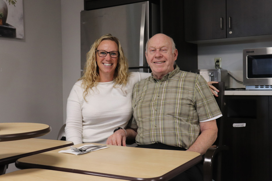 Jennifer Field in a cream sweater sits with Veteran Joseph "Lou" Warren in a plaid shirt at a dining table