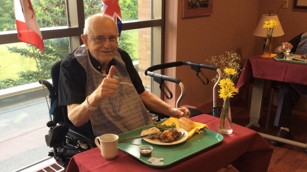 An elderly man gives a thumbs up before enjoying his meal