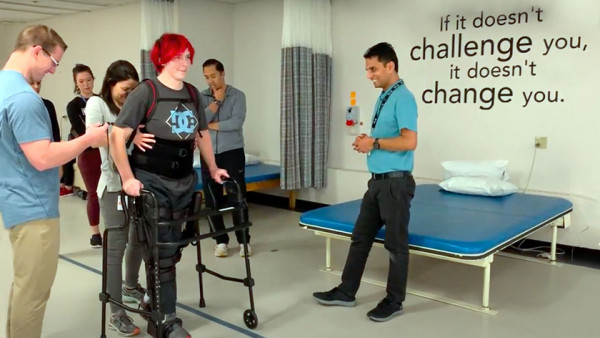 teenaged patient walking with a walker surrounded by mobility staff